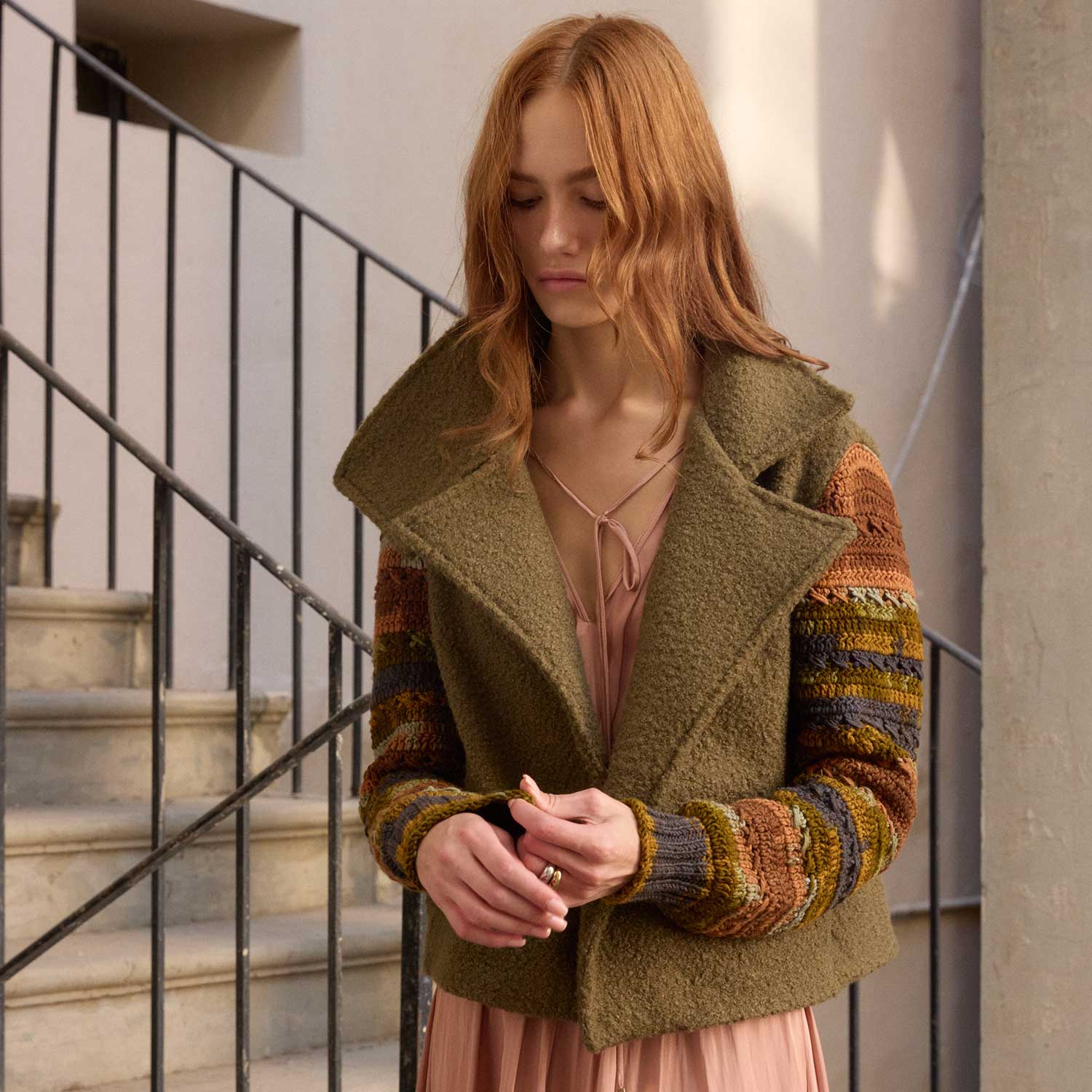 Woman wearing a green coat with patterned sleeves standing in an indoor setting.