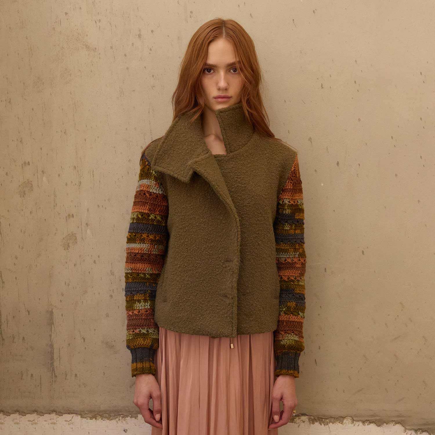 Woman wearing a green vest over a patterned sweater with a beige background