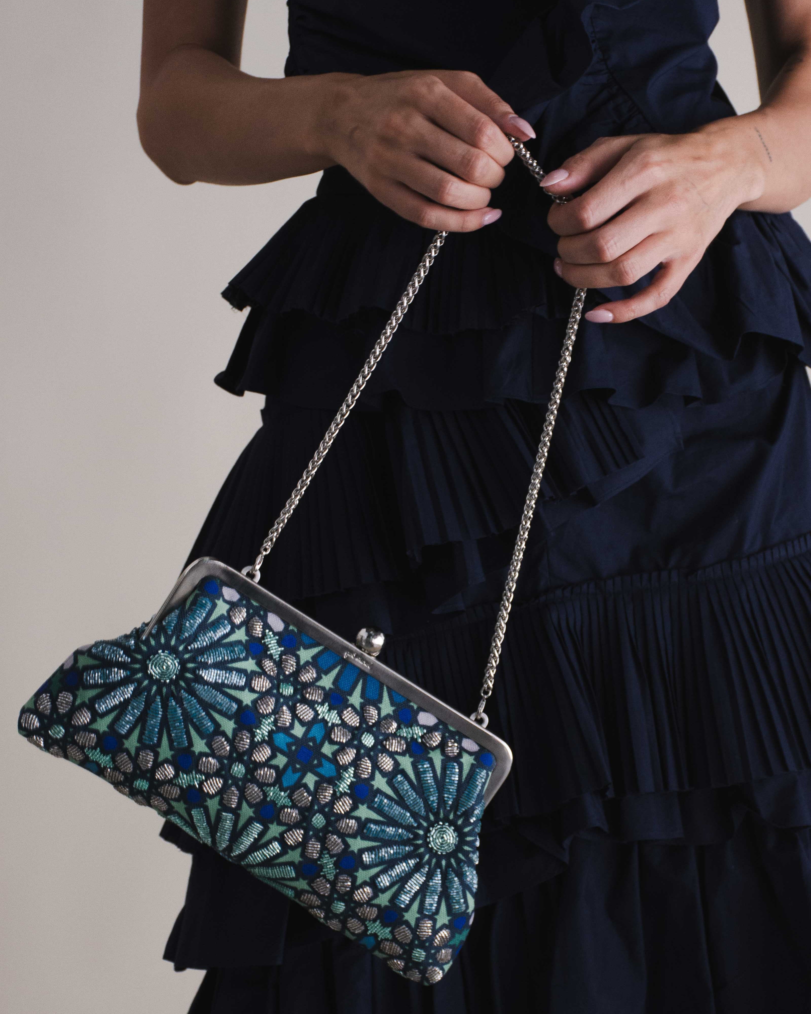 Person wearing a dark blue dress holding a decorative blue handbag.
