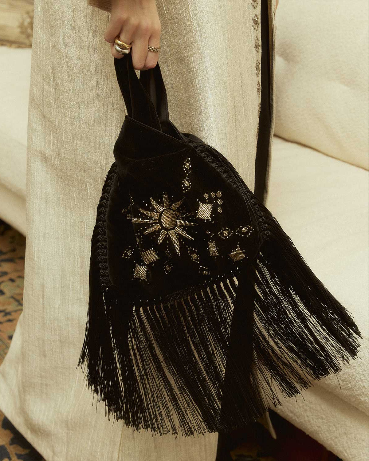 Black hand beaded slip bag with fringes held by a person wearing a long beige garment.