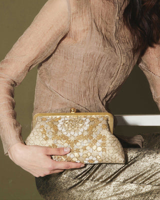 Person holding a gold and white arabesque patterned clutch bag against a neutral background
