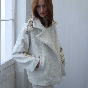Woman wearing a white textured jacket
with floral details in a minimalistic setting.