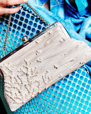 Silver pearl clutch bag on a blue textured surface
