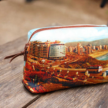 A zippered pouch with a printed scenic photograph of a coastal city, resting on a rustic wooden surface.