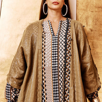 A person wearing an olive-colored abaya with hand-crocheted details on the front lapels and sleeve slits, standing in front of a golden background.