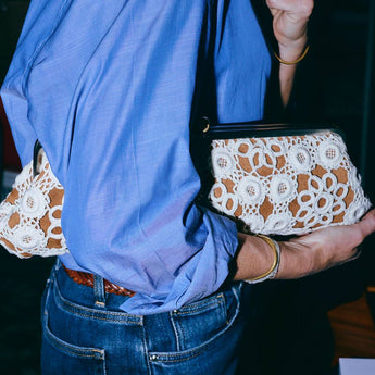 Person holding a clutch with white lace design, wearing a blue shirt and jeans.