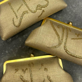 Three customized gold handbags with gold embroidery on a dark surface