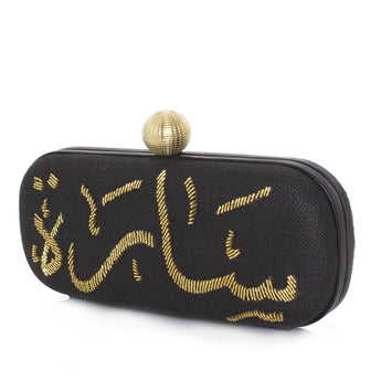 A black clutch with gold calligraphy geometric patterns and a gold clasp on a white background.