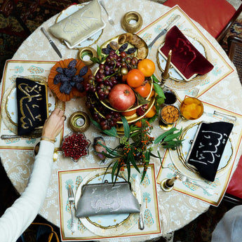 Decorative table setting with fruit, candles, and place mats on a round table.