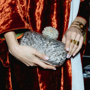 Person holding a silver gold clutch, wearing gold rings and bracelets.
