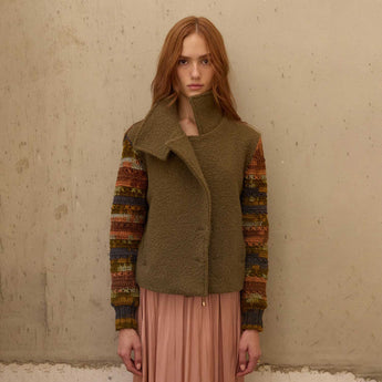 Woman wearing a green vest over a patterned sweater with a beige background