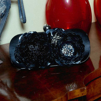 Black clutch bag with floral embellishments and beads on wood.