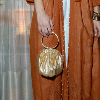 Person wearing an orange dress holding a gold round bracelet bag with a ring handle.