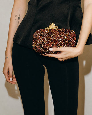 Person holding a beaded clutch with a decorative clasp against a neutral background