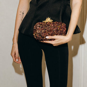 Person holding a beaded clutch with a decorative clasp against a neutral background