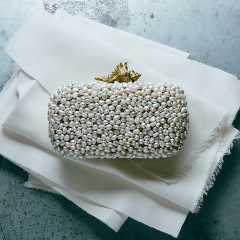 Pearl embellished clutch bag on a white fabric surface with a textured gray background