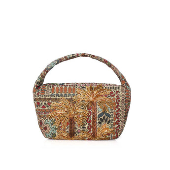 A small handbag with a curved top handle, covered in dense batik-style fabric featuring palm tree motifs and multicolored floral patterns in orange, brown, red, beige, and teal on a white studio background.