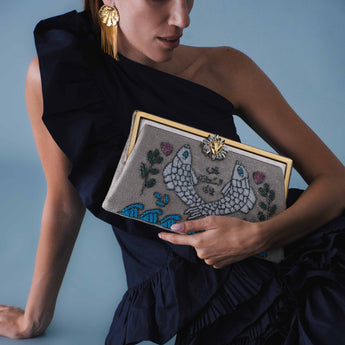 Woman holding a decorative clutch with intricate designs against a blue background