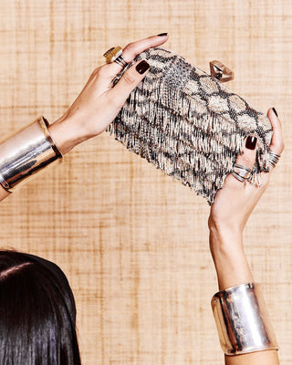 Beaded keffiyeh design clutch with fringes detail between the hands of a model.