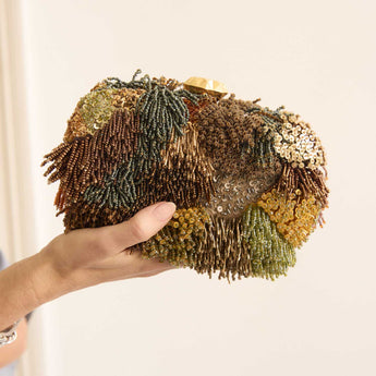 Hand holding Full beaded clutch bag with intricate designs on a white background