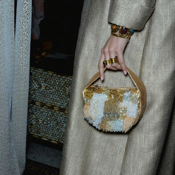 Person holding a gold and white beaded handbag with a textured wall in the background