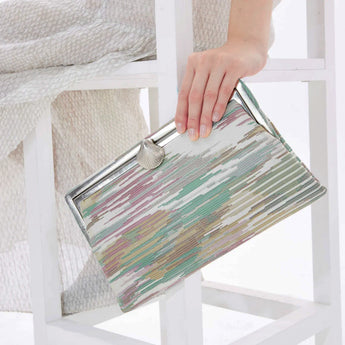Multicolored pastel clutch bag held by a hand on a white chair