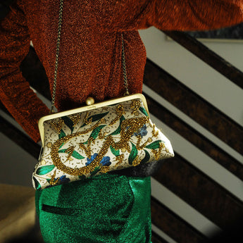 A model holding a clutch handbag with a floral pattern and gold-colored beads forming a text hobb that means love.