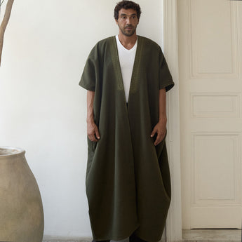 Man wearing a green abaya over a white shirt in a minimalistic setting