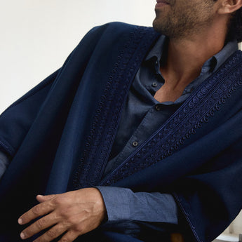 Man wearing a dark blue embroidered abaya over a matching shirt against a white background
