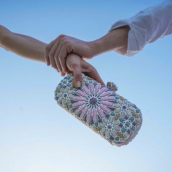 Two hands holding a multicolored moroccan patterned clutch bag on a white background