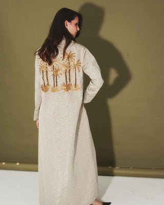 A model wearing a beige honeycomb fabric cover-up with hand-beaded golden palm tree motifs.