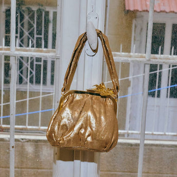 Gold handbag hanging on a white metal gate