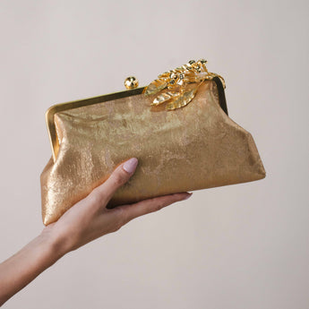 Gold clutch held by a hand against a plain background
