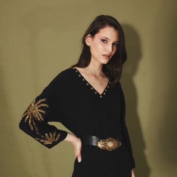 Woman wearing a black dress with gold embellished palm tress against a green backdrop