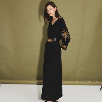 Woman wearing a black dress with gold embellished palm tress against a green backdrop