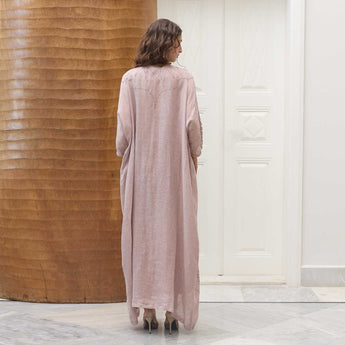 Woman wearing a long abaya embroidered with beads in a room with wooden walls.