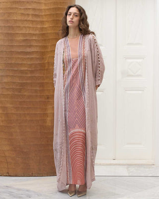 Woman wearing a long, pastel patterned dress with a matching abaya in a room with wooden walls.