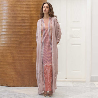 Woman wearing a long, pastel patterned dress with a matching abaya in a room with wooden walls.
