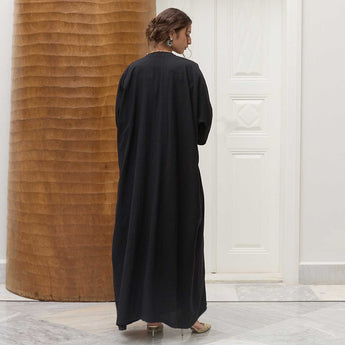 Woman wearing a black abaya in an indoor setting with a wooden wall and white door.