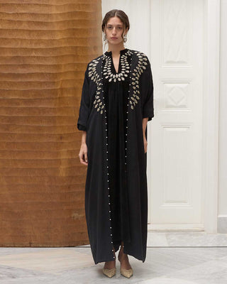 Woman wearing a black dress with intricate petals in a room with wooden paneling and a white door.