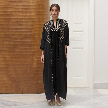 Woman wearing a black dress with intricate petals in a room with wooden paneling and a white door.