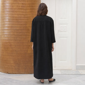Woman wearing a black cotton amira dress with a decorative  beaded petal neckline in a minimalistic setting.