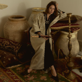 Woman wearing a abaya embroidered with petals standing in a room with decorative elements and a mirror.