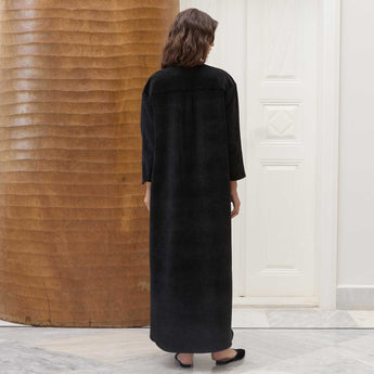 Woman wearing a Amira black dress standing in a room with a textured wall and white door.