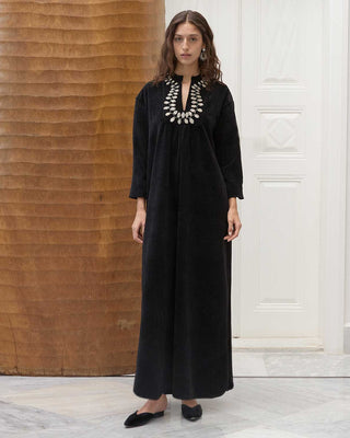 Woman wearing a black amira dress with a textured wall and white door in the background