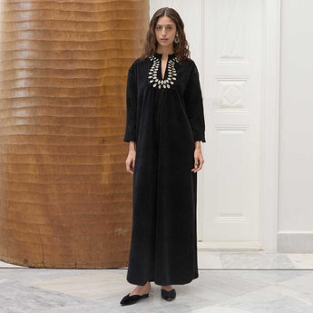 Woman wearing a black amira dress with a textured wall and white door in the background