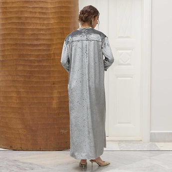 Woman wearing a long, gray amira dress with intricate detailing in a minimalistic setting.