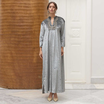 Woman wearing a long, gray amira dress with intricate detailing in a minimalistic setting.