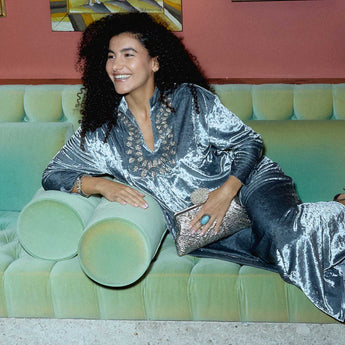 Woman in a silver outfit sitting on a green couch with a painting in the background