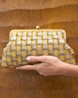 Hand holding a woven gold clutch against a wooden background
